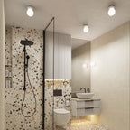 Plafonniers Zori en céramique émaillée blanche au plafond d'une salle de bains en terrazzo avec deux appliques de la même ligne près du miroir