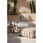 Plaid en coton écru posé sur une banquette près d'un pouf rayé et de cactus