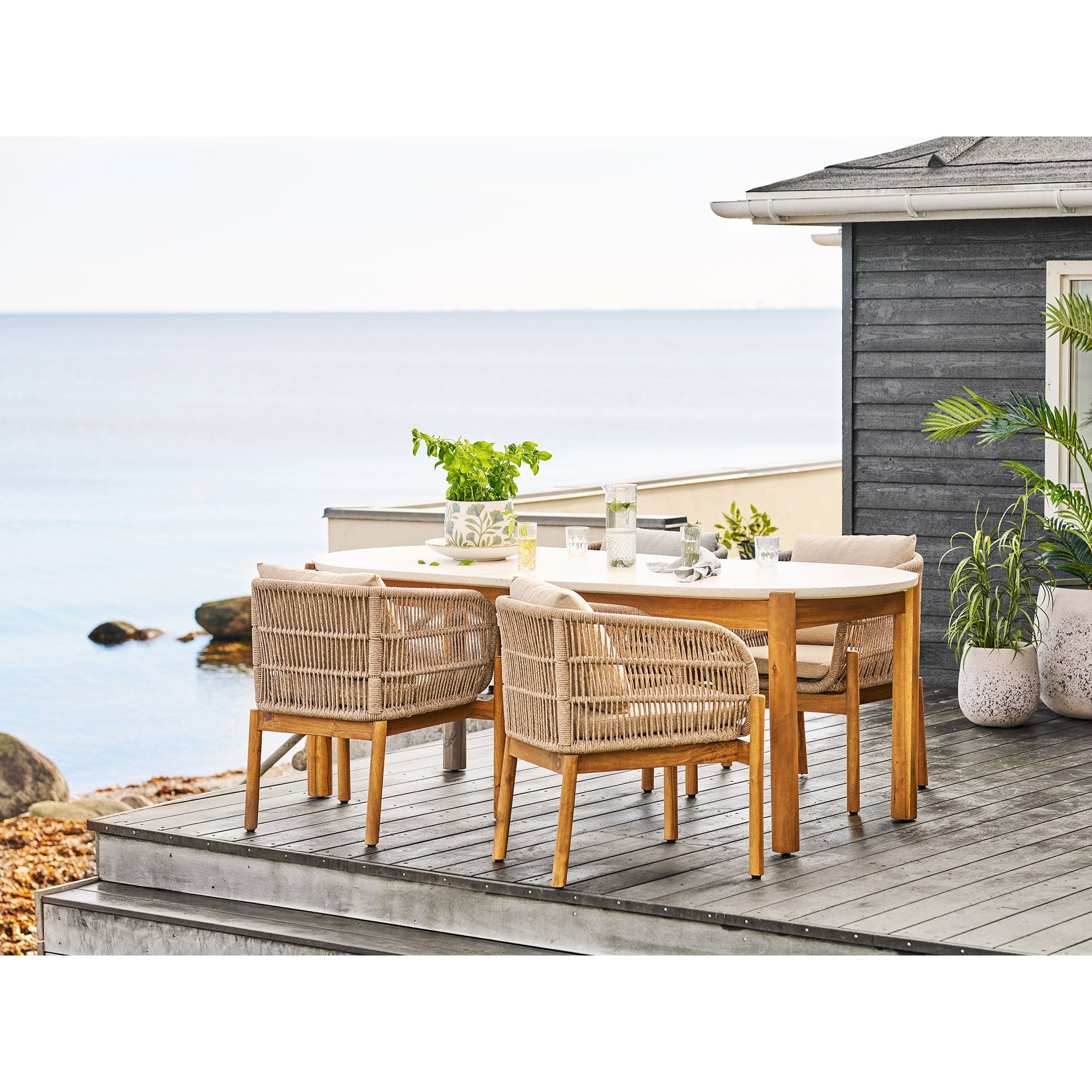 Plante herbe artificielle verte en pot sur terrasse bois bord de mer avec salon de jardin rotin et table blanche