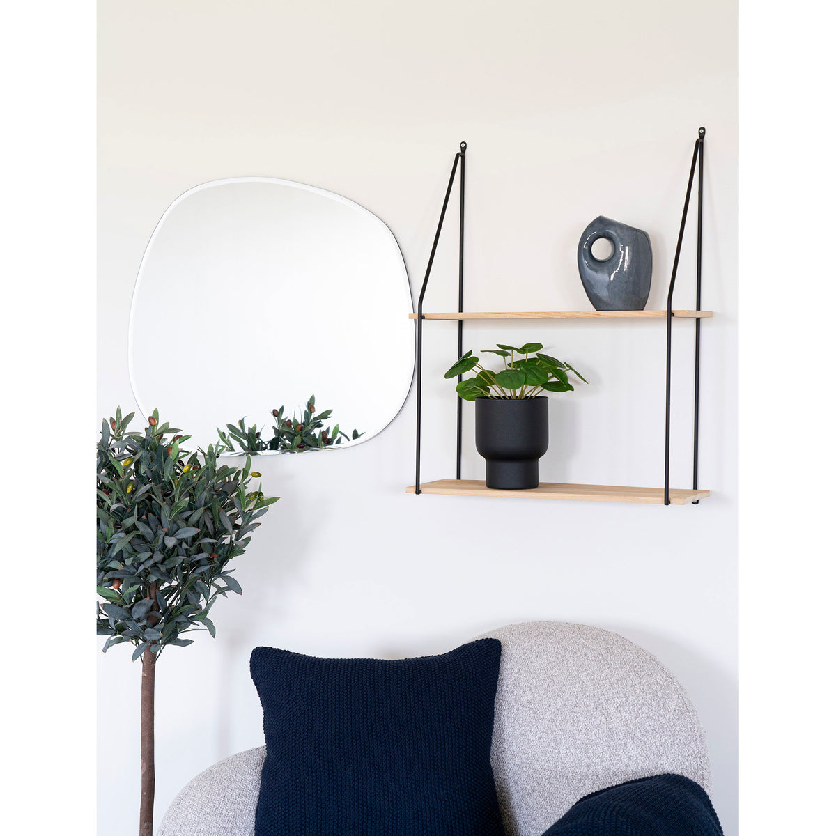 Pilea peperomioides artificiel dans un pot noir sur une étagère murale en bois près d'un miroir organique