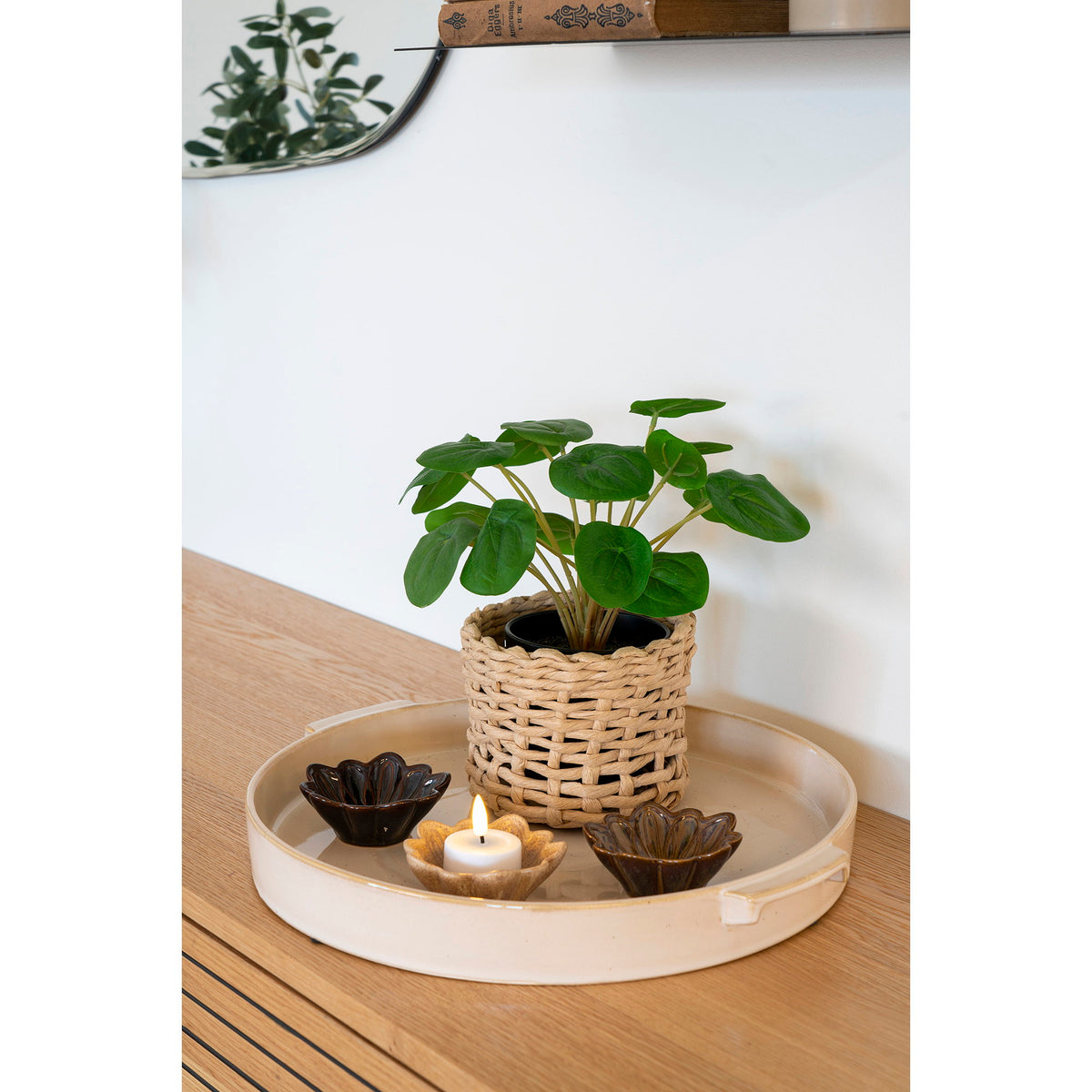 Pilea peperomioides artificiel dans un panier tressé sur un plateau en céramique avec des bougies