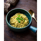 Plat à manche en grès bleu vert garni de risotto au persil sur une table en bois sombre avec une cuillère dorée
