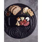 Plat à tapas en terre cuite noircie garni de fromages et de charcuterie sur un plateau en bois noir