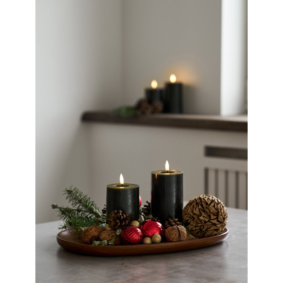 Plateau en acacia en centre de table avec deux bougies vertes des pommes de pin et des boules rouges