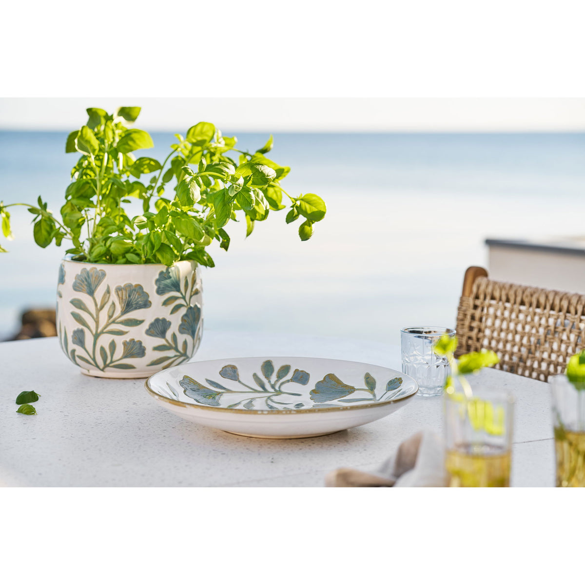 Plateau floral en céramique sur une table blanche à côté d'un cache-pot garni de basilic