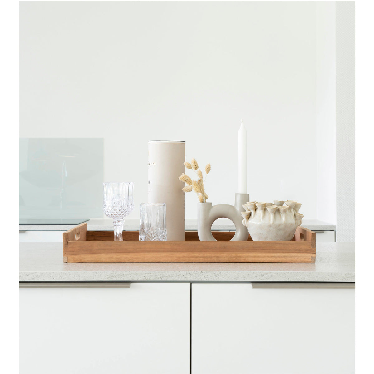 Plateau Faro en teck posé sur un plan de travail blanc avec verres bougeoir et vase