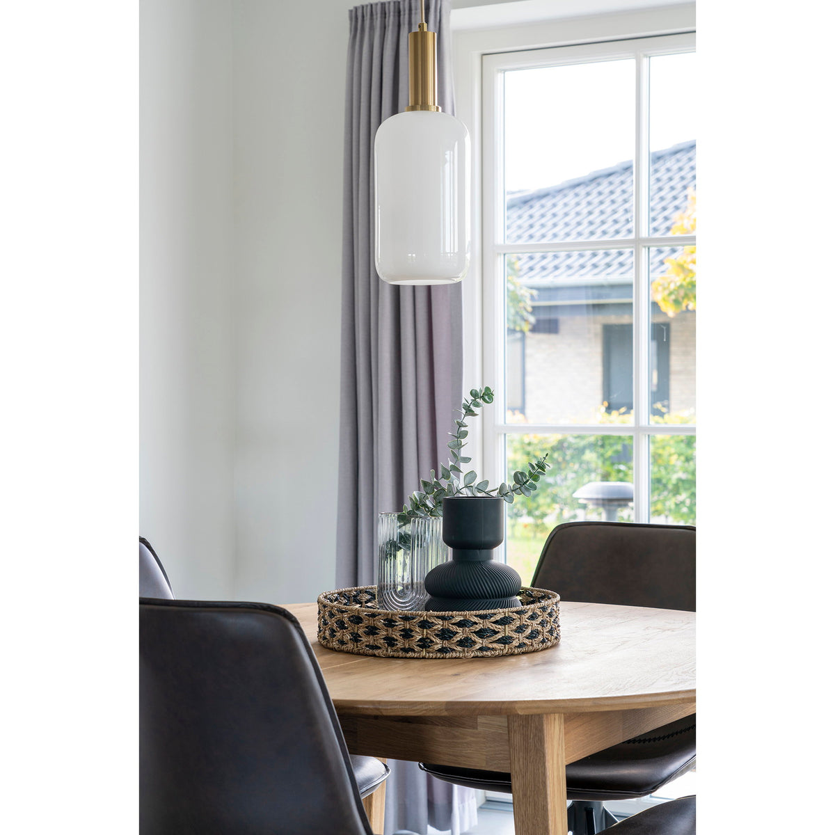 Plateau Nerja avec un vase noir et de l'eucalyptus sur une table ronde en chêne sous une suspension en verre blanc