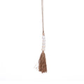 Pompon décoratif Cone suspendu à son cordon avec cinq coquillages blancs empilés et une jupe de fibres végétales sur fond blanc