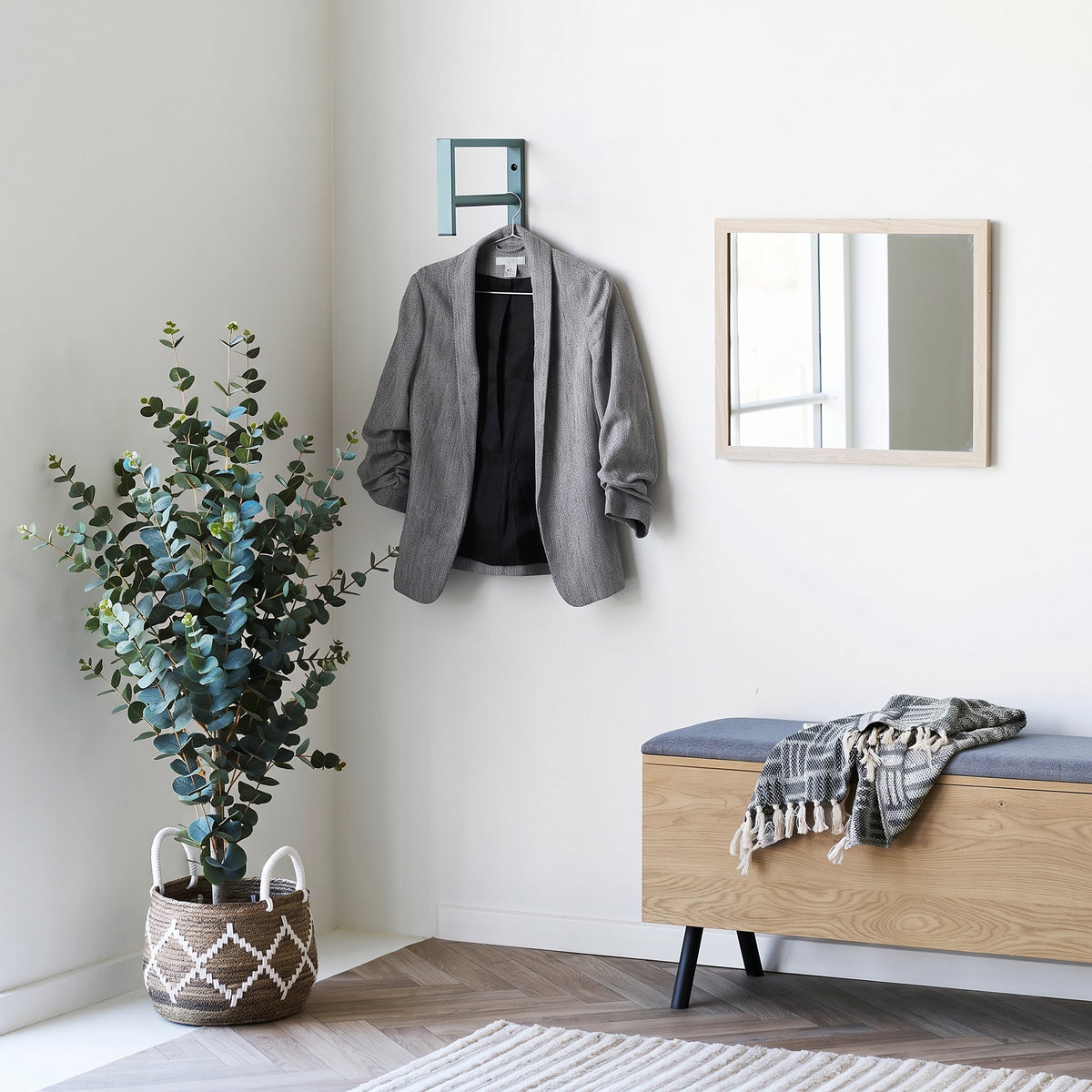 Porte-manteau Trento vert sauge avec une veste grise sur la barre, à côté d'un miroir au cadre bois