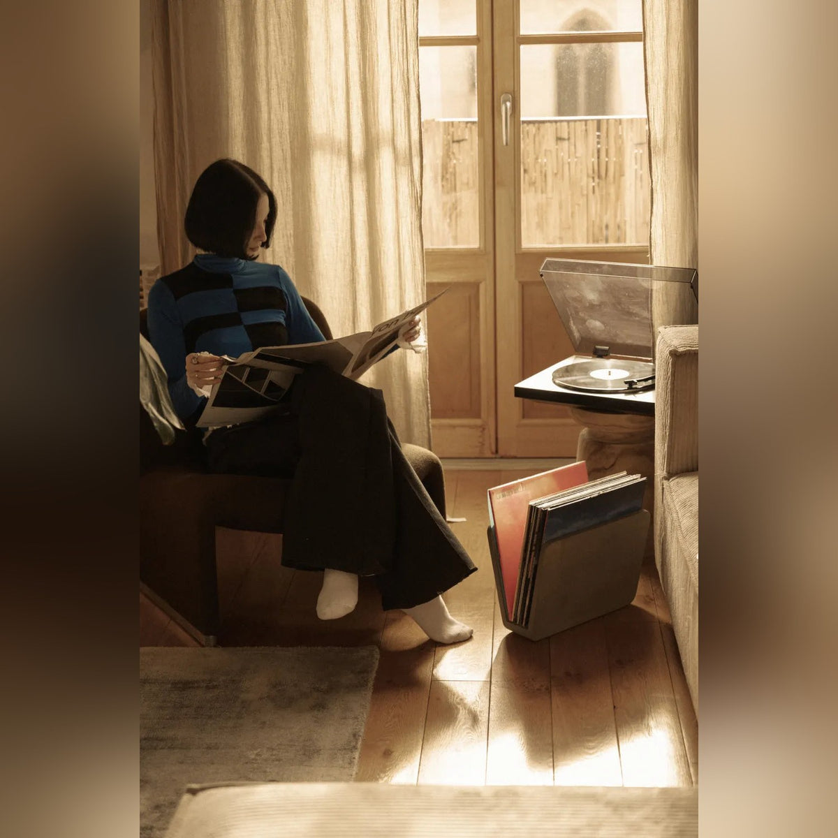 Femme lisant le journal dans un fauteuil à côté du porte-revues Doc en béton garni de vinyles