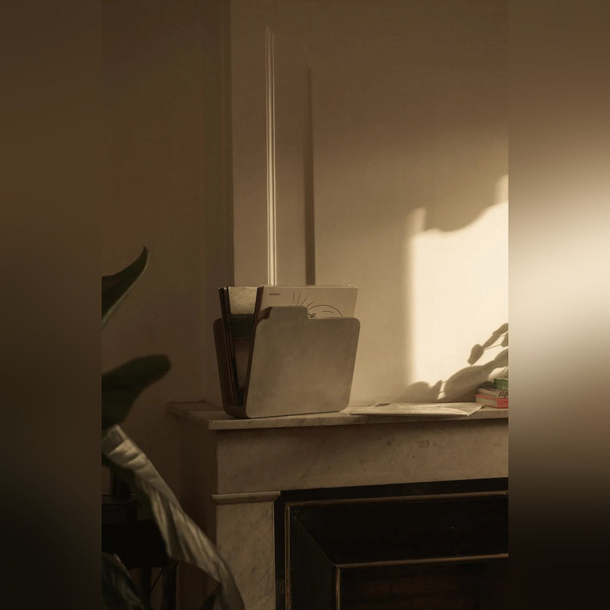 Porte-revues Doc en béton sur une cheminée en marbre dans une lumière rasante