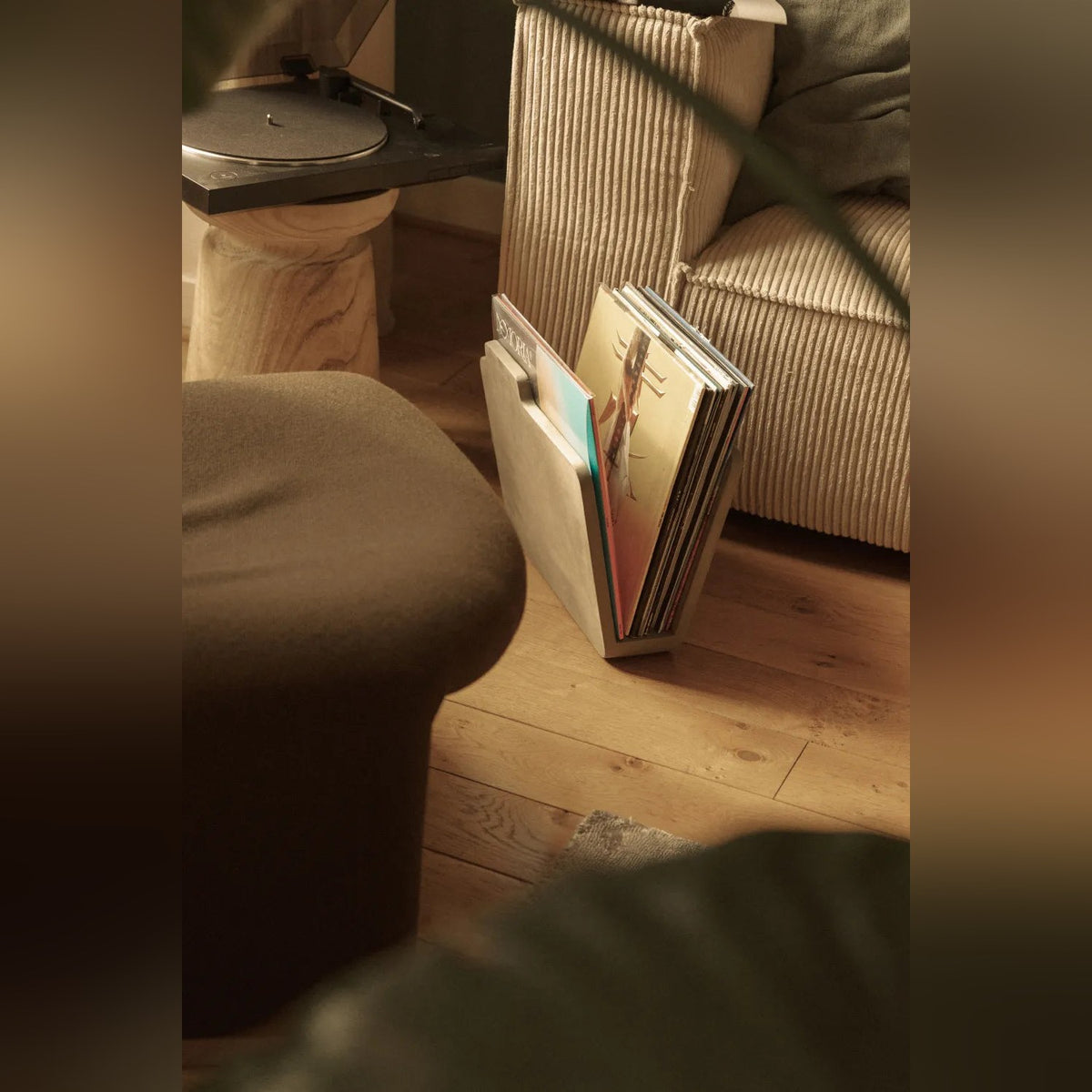 Vue plongeante sur le porte-revues Doc en béton garni de vinyles au pied d'un canapé en velours côtelé