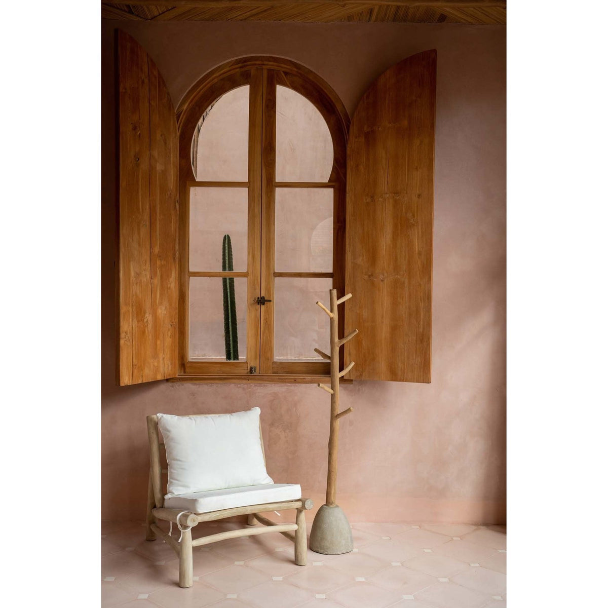 Portemanteau en teck et béton à côté d'une chaise basse en teck sous une fenêtre cintrée à volets de bois