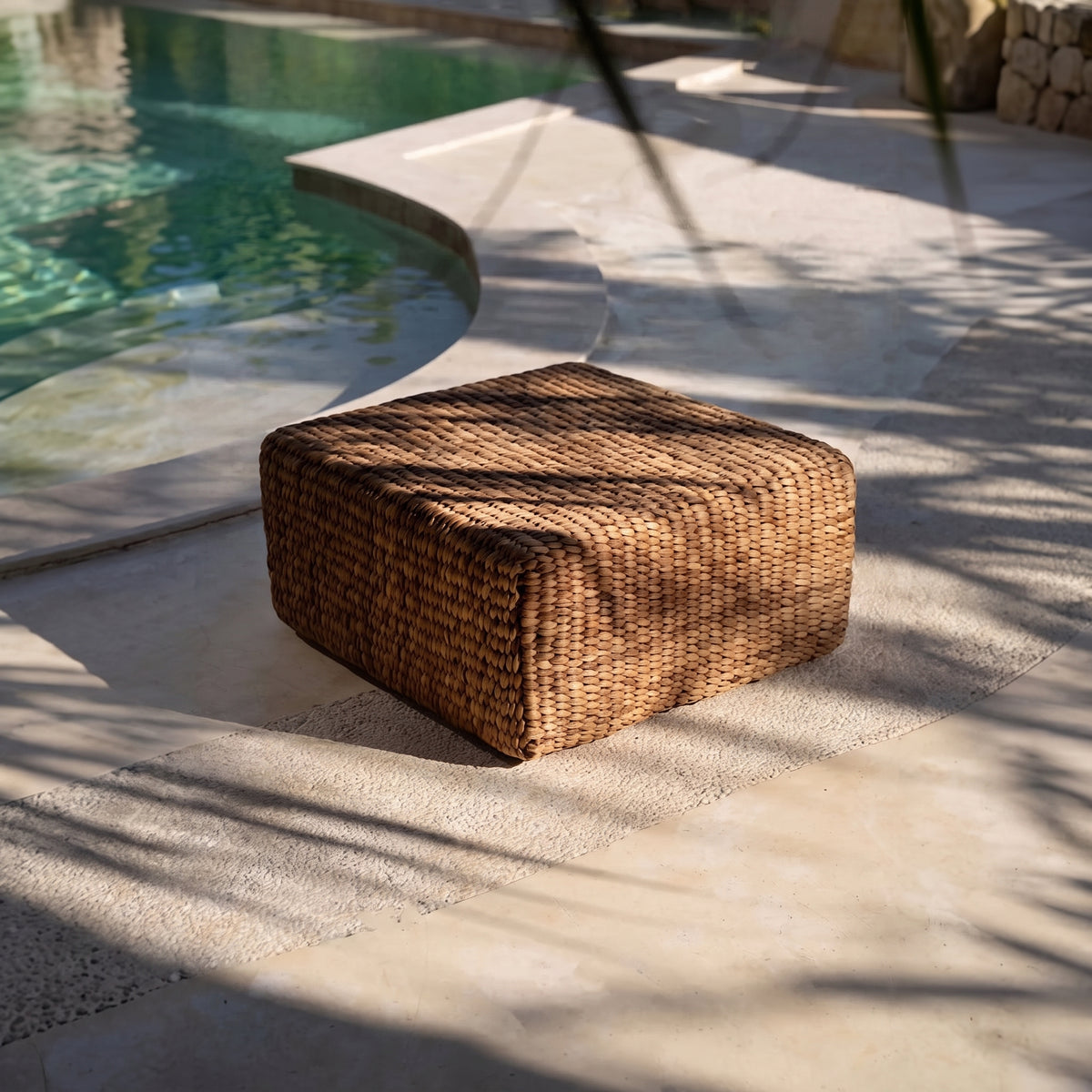 Pouf carré en jacinthe d'eau tressée au bord d'une piscine, à l'ombre des palmes