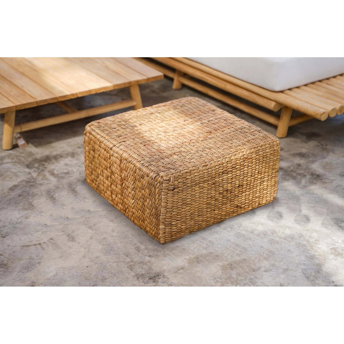 Pouf carré en jacinthe d'eau entre une table basse et un canapé sur un sol en béton