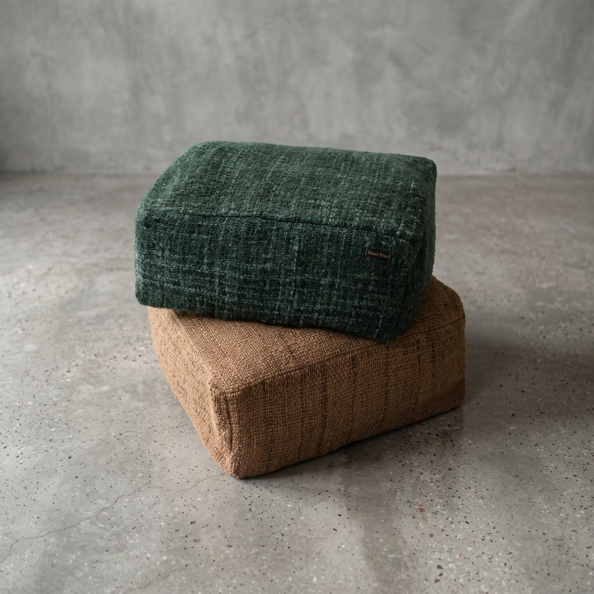 Pouf carré Oh My Gee vert forêt posé sur un pouf carré en coton tissé brun, sur un sol en béton