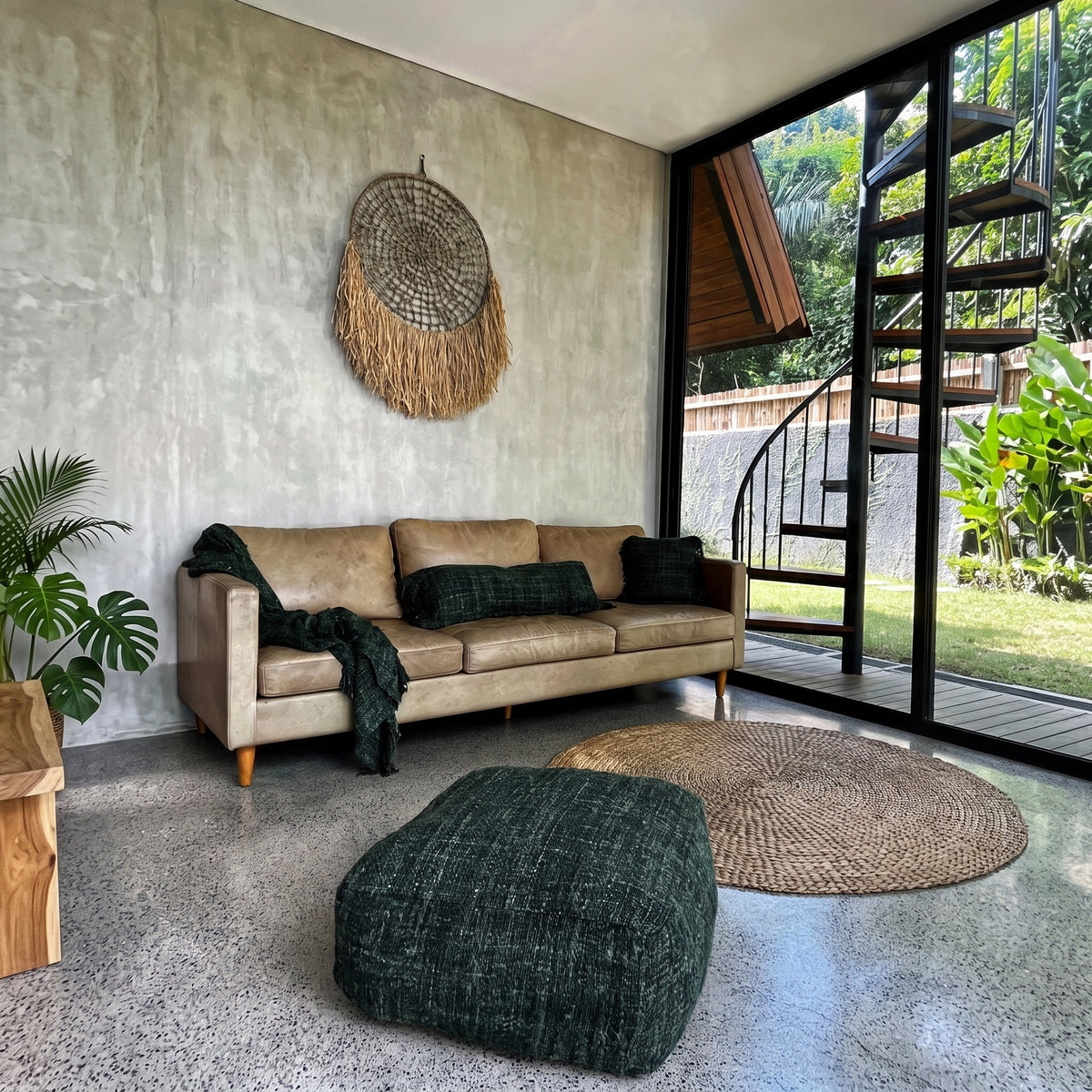 Pouf carré Oh My Gee en coton tissé vert forêt sur un sol en béton ciré, entre un canapé en cuir et une baie vitrée ouverte sur le jardin