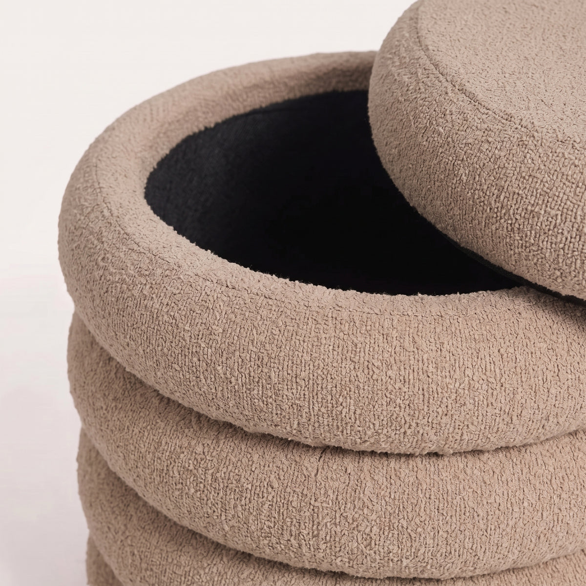 Gros plan du rangement intérieur noir du pouf, couvercle en bouclé beige posé de côté