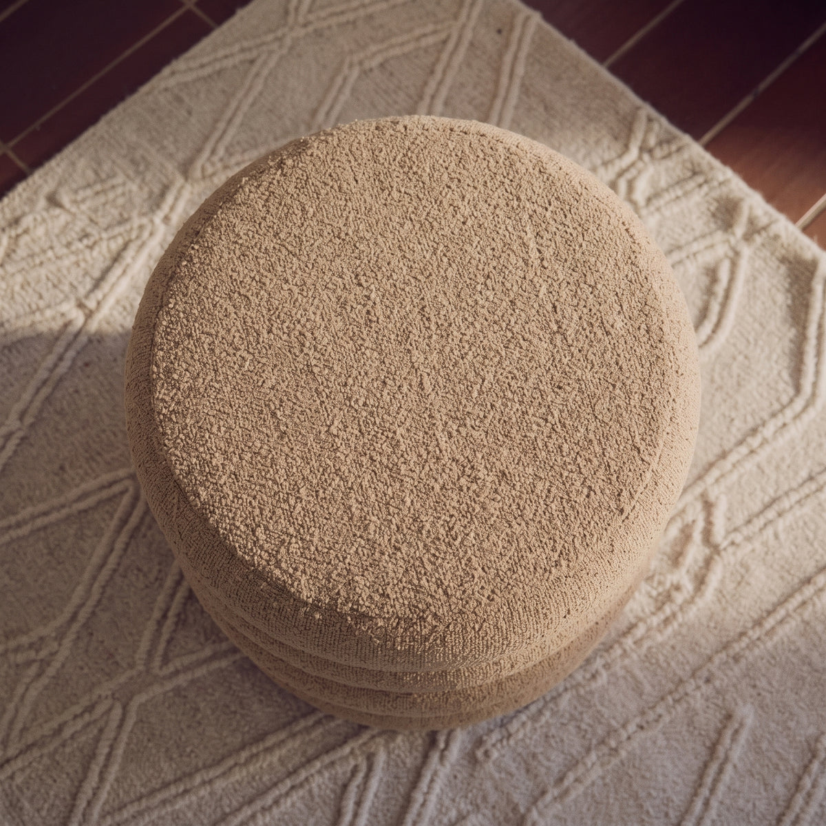 Dessus rond du pouf en bouclé beige vu d'en haut, posé sur un tapis crème à motif en relief