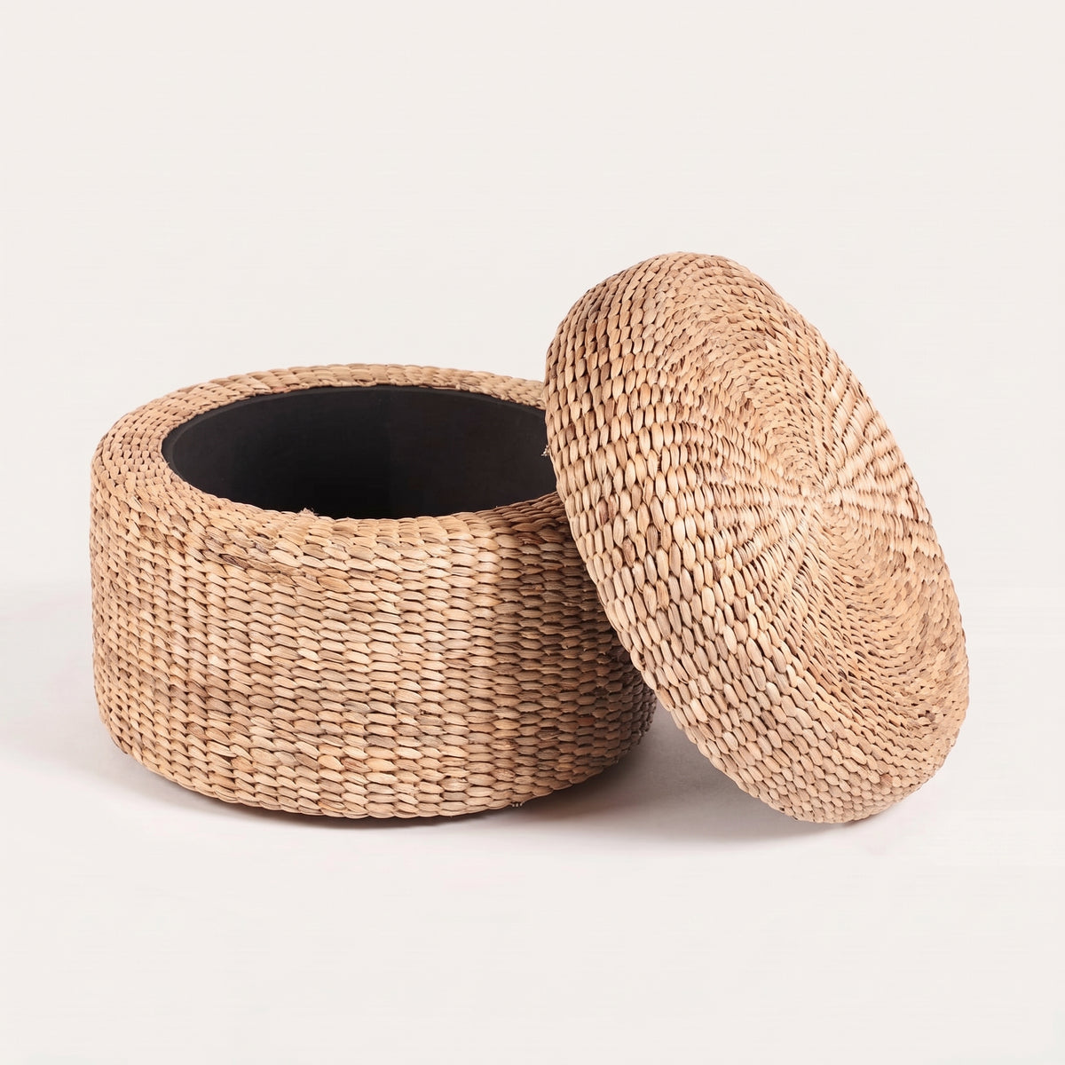 Pouf coffre rond en jacinthe d'eau tressée, couvercle posé à côté, laissant voir l'intérieur noir du rangement