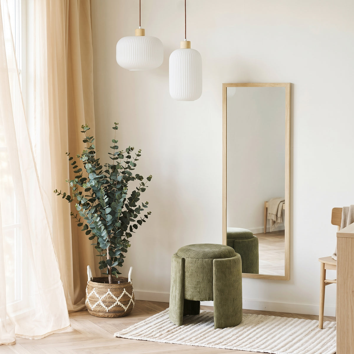 Pouf coffre Walsdorf vert olive devant un miroir au cadre bois, près d'un eucalyptus et de deux suspensions blanches