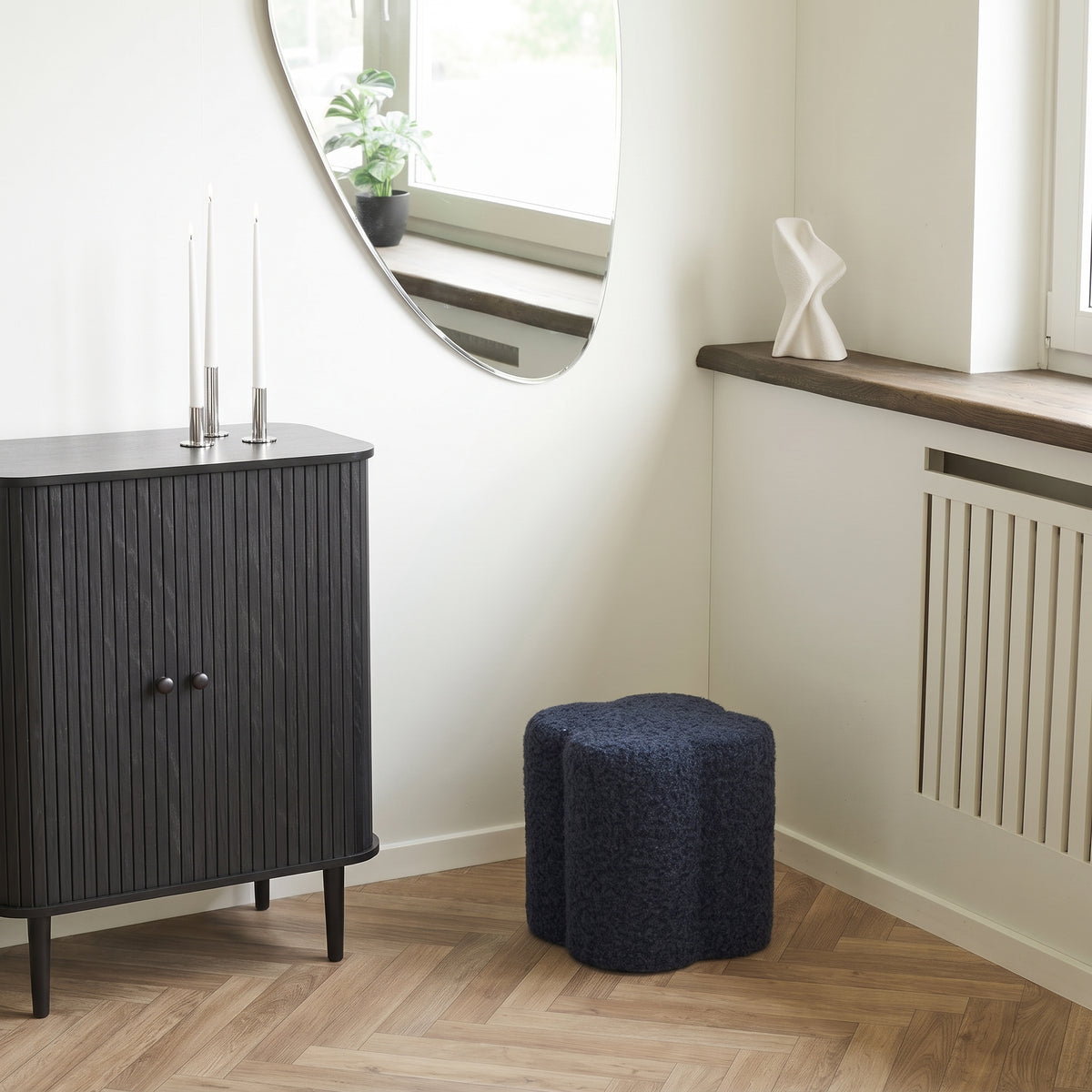 Pouf Durban bouclé bleu marine sur un parquet à bâtons rompus, près d'un buffet noir à lamelles et sous un miroir