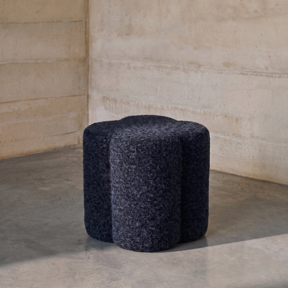 Pouf Durban bouclé bleu marine dans l'angle d'une pièce aux murs et au sol en béton