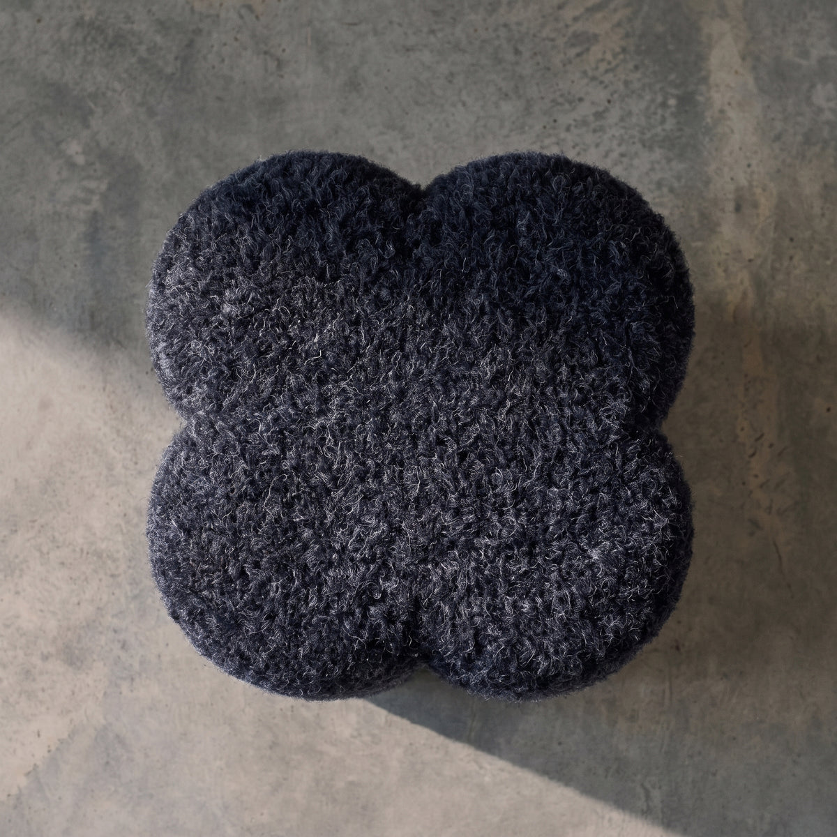 Assise en forme de trèfle du pouf Durban bouclé bleu marine, vue de dessus sur un sol en béton