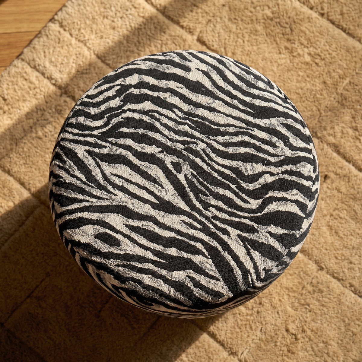 Dessus rond du pouf en jacquard zébré vu d'en haut, posé sur un tapis beige