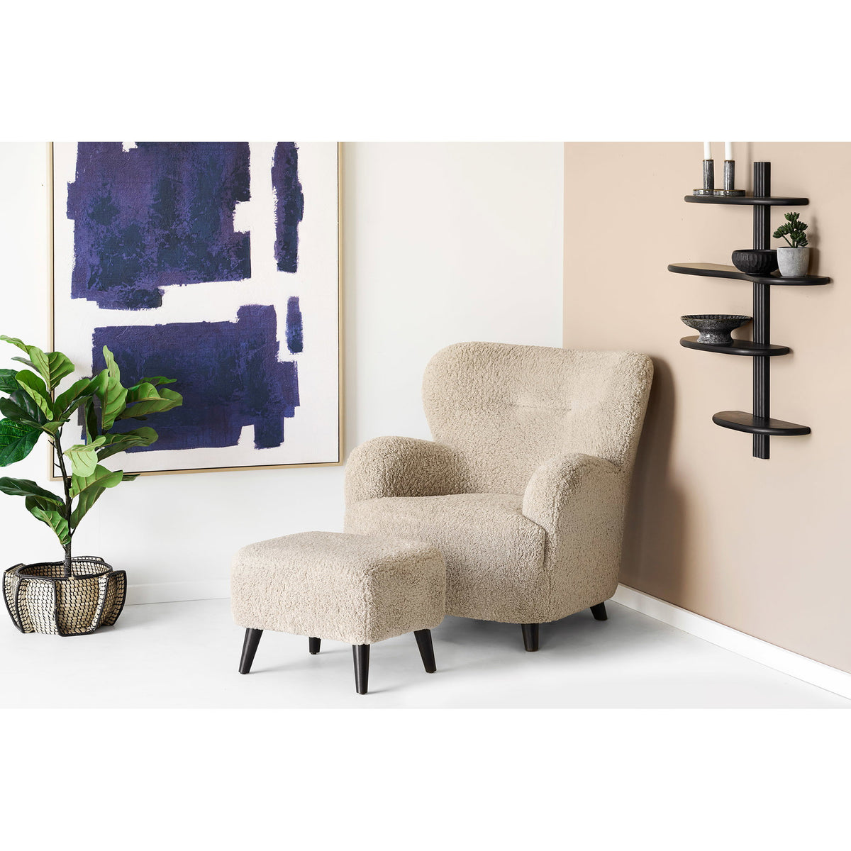 Pouf Lunaro en bouclé beige devant un fauteuil assorti dans un salon clair avec plante et étagère murale noire