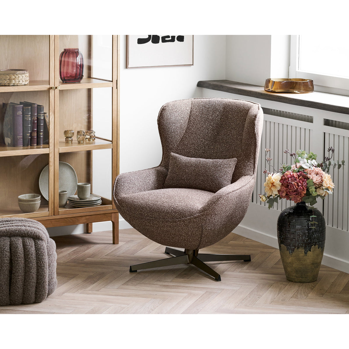 Pouf Napier marron au premier plan d'un coin lecture avec un fauteuil brun et une vitrine en bois
