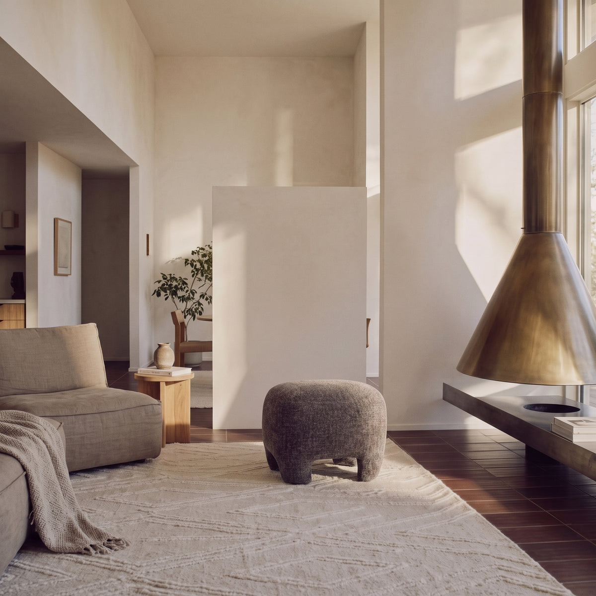 Pouf Nazare en tissu gris chiné dans un séjour lumineux, entre un canapé en lin et une cheminée en laiton