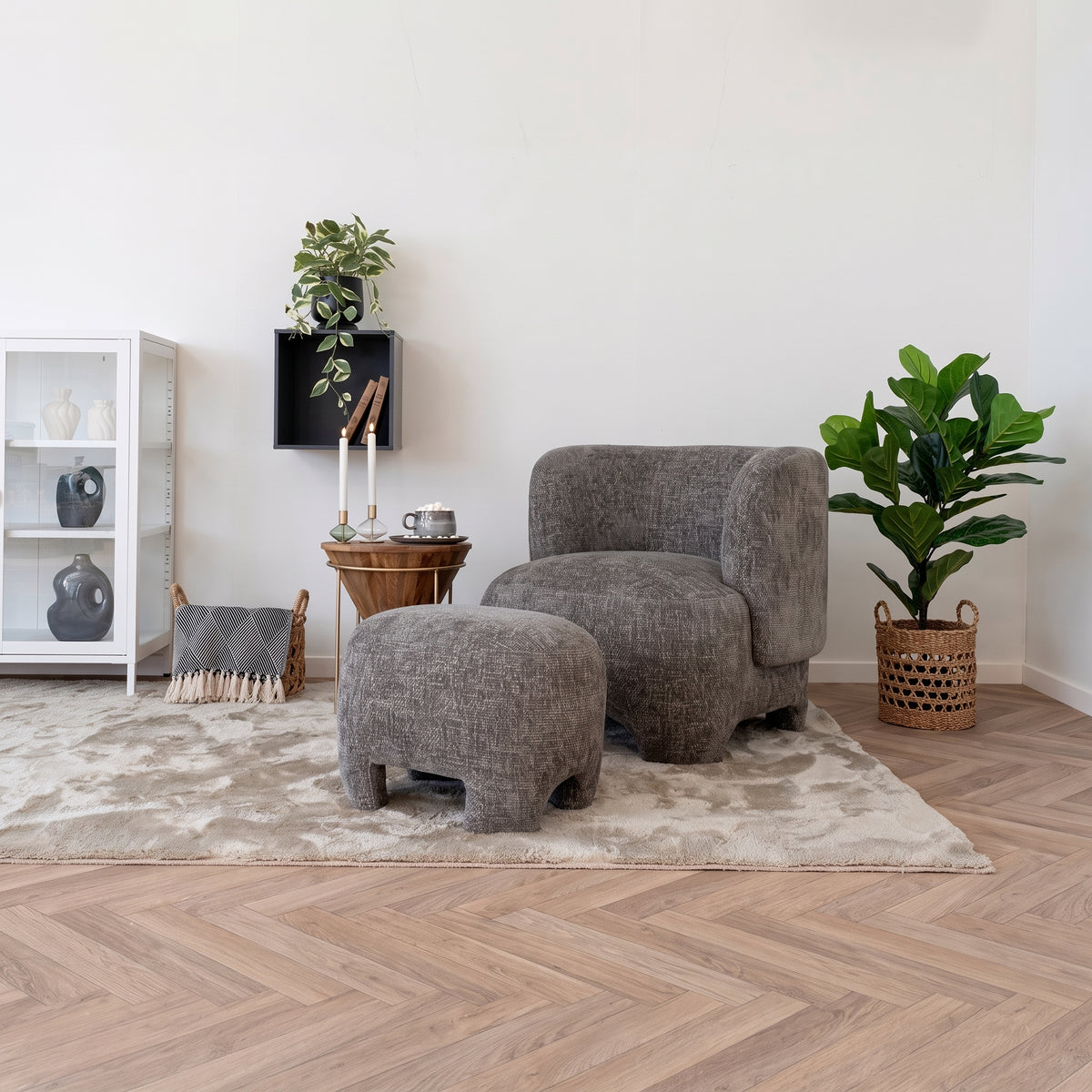 Pouf Nazare en tissu gris chiné devant un fauteuil assorti, sur un tapis clair dans un salon