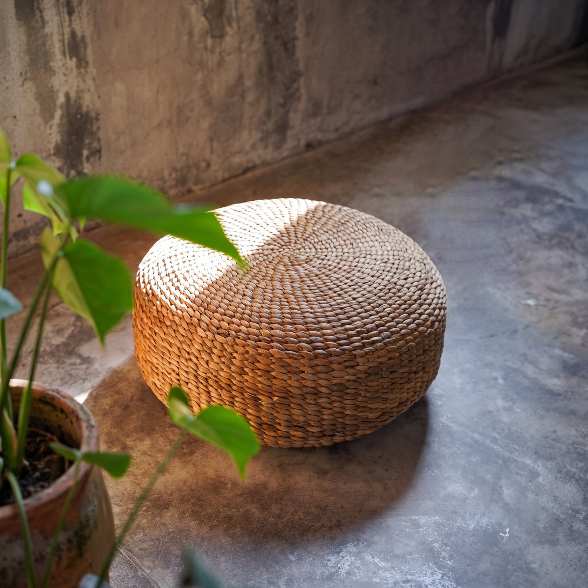 Pouf rond en jacinthe d'eau tressée au tressage en spirale, sur un sol en béton près d'une plante en pot