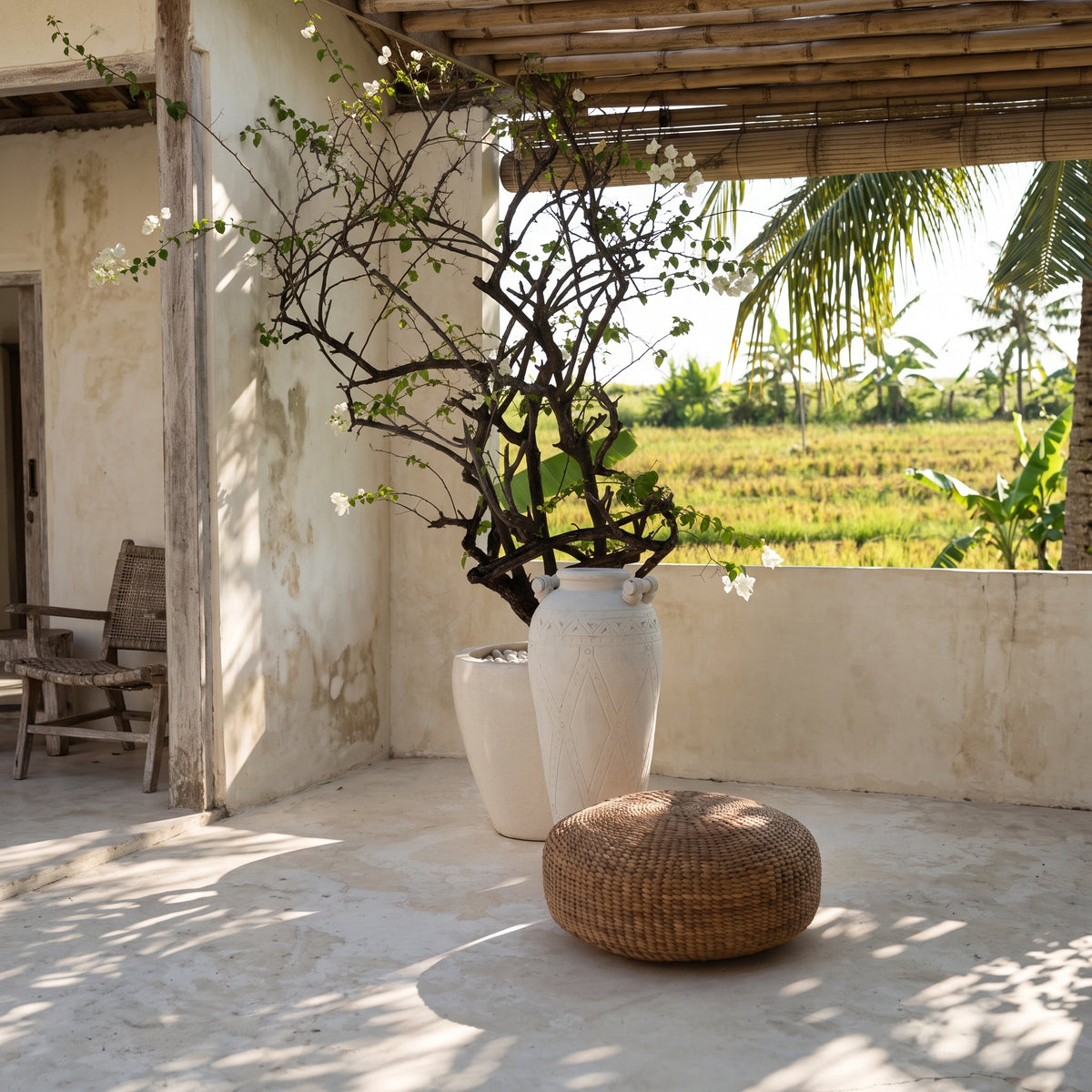 Pouf rond en jacinthe d'eau tressée sous une pergola en bambou, près d'une jarre blanche face aux rizières
