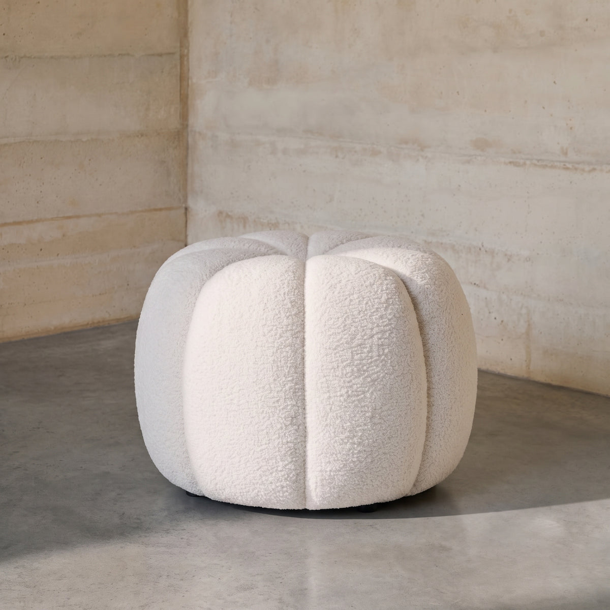 Pouf rond Paisley en teddy blanc cassé dans l'angle d'une pièce aux murs et au sol en béton