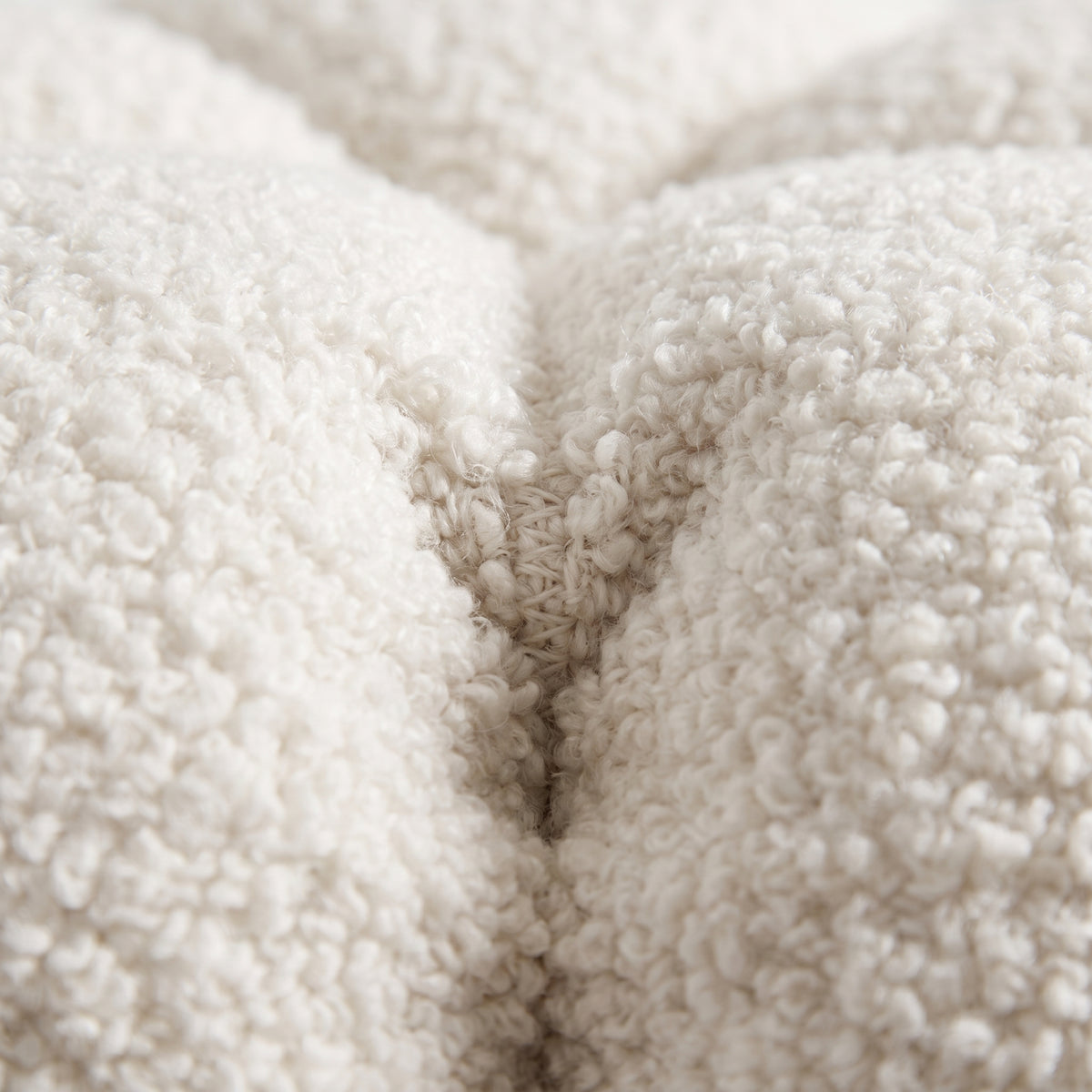 Gros plan sur la bouclette dense du teddy blanc cassé et une couture du pouf Paisley