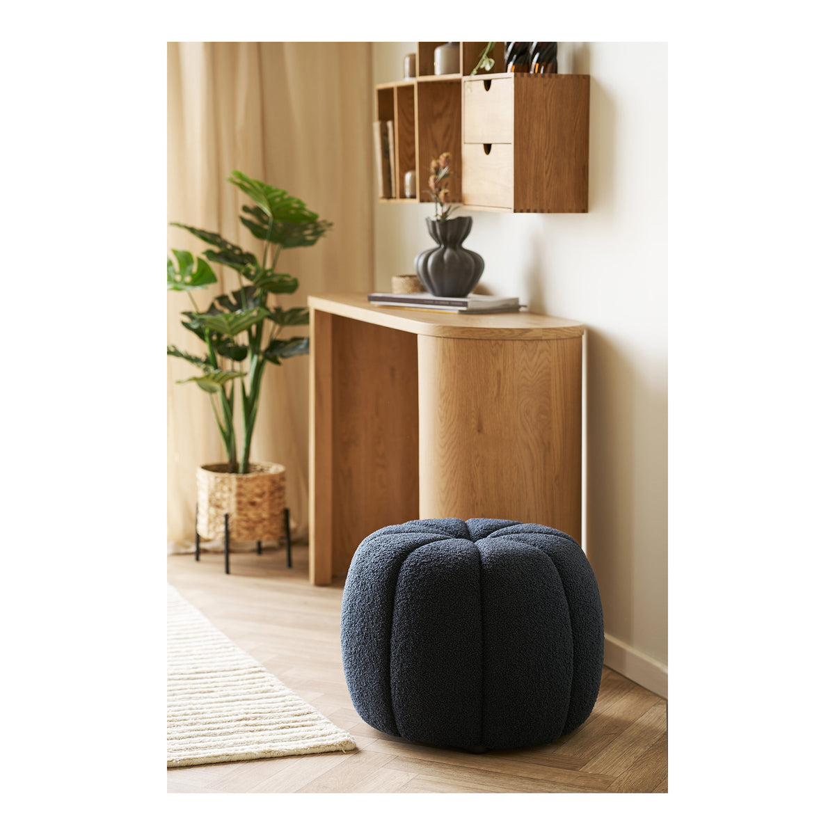 Pouf Paisley teddy bleu marine sur un parquet en chevrons devant une console en bois clair et une étagère murale en bois