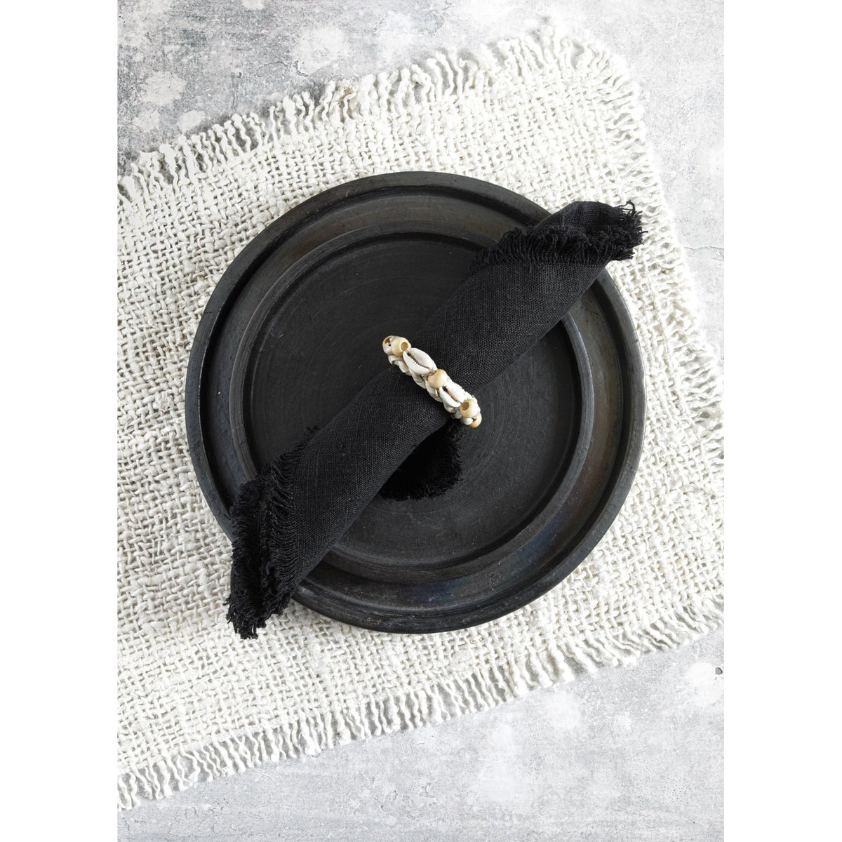Rond de serviette à coquillages sur une serviette noire roulée posée dans une assiette sombre