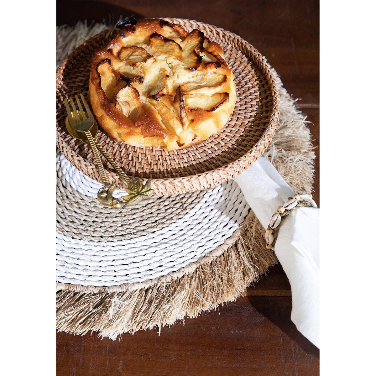 Serviette en lin blanc tenue par un rond de serviette à coquillages à côté d'un gâteau aux pommes