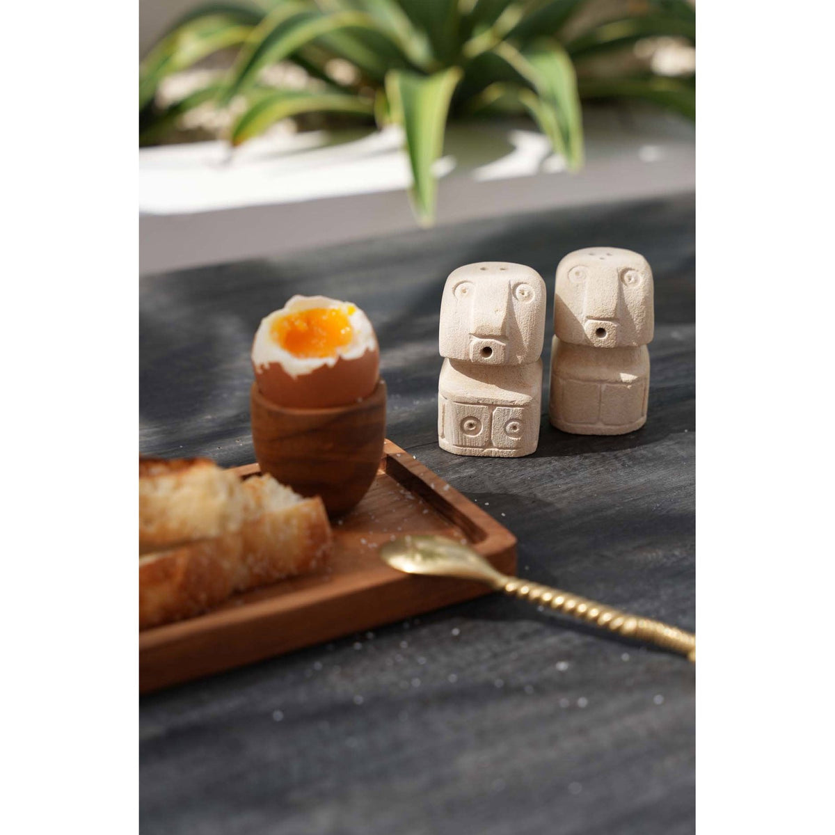 Salière et poivrière Sumba en pierre de grès près d'un œuf à la coque et de mouillettes sur une table sombre