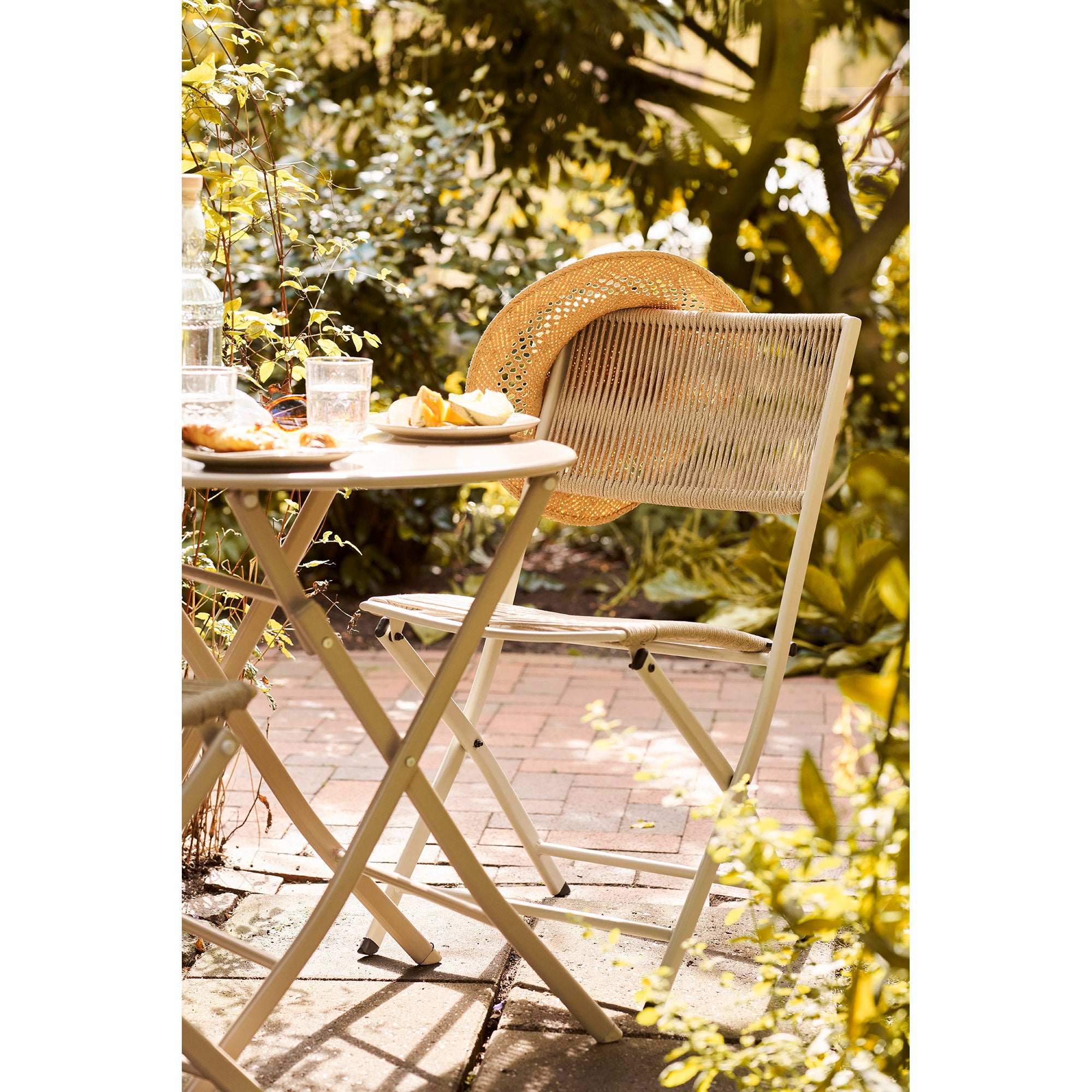 Chaise bistro Arcas taupe en jardin fleuri avec chapeau de paille posé sur le dossier