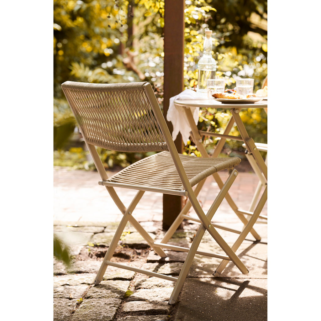 Vue dos chaise Arcas taupe en jardin, table bistro ronde et végétation en arrière-plan