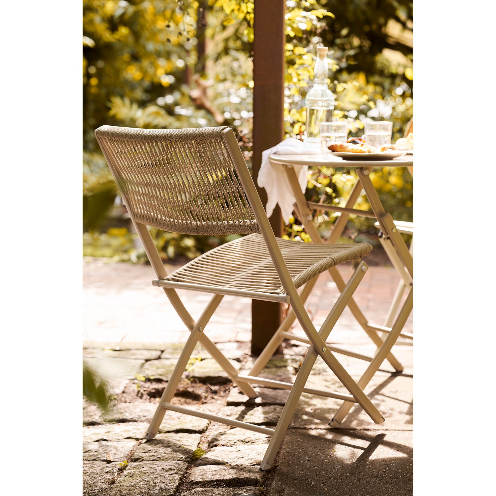 Vue dos chaise Arcas taupe en jardin, table bistro ronde et végétation en arrière-plan