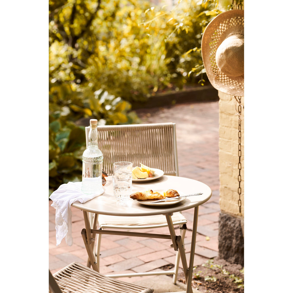 Détail table ronde Arcas taupe avec petit-déjeuner, croissants et carafe en terrasse