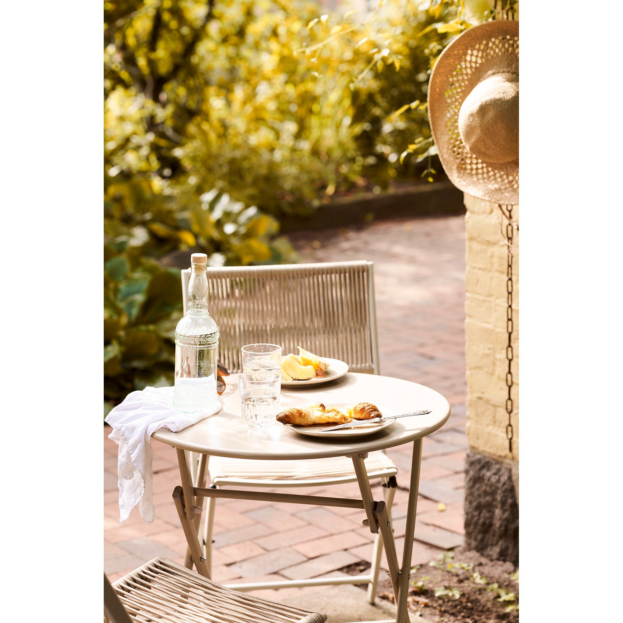 Détail table ronde Arcas taupe avec petit-déjeuner, croissants et carafe en terrasse