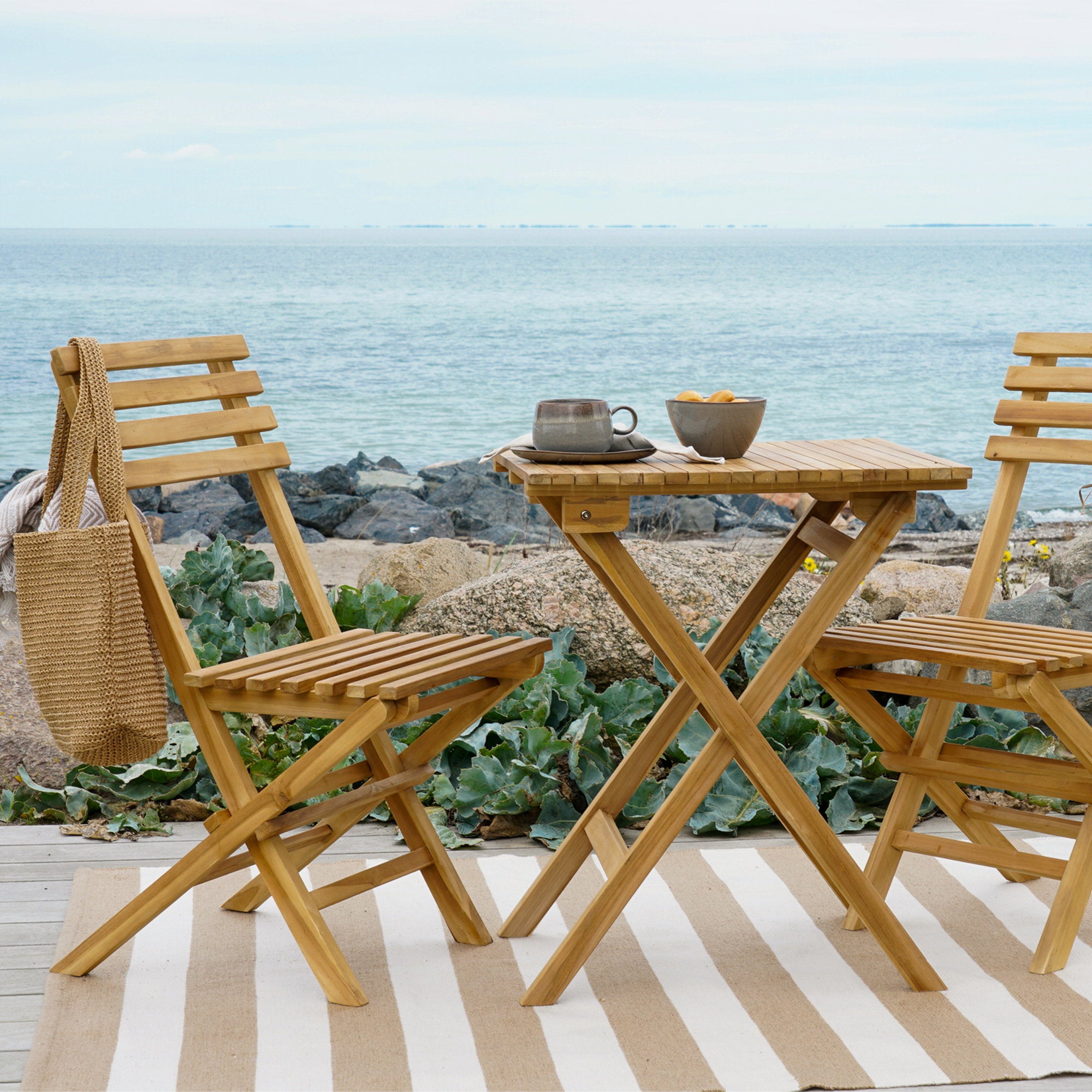 Salon bistro Cuenca teck naturel sur terrasse bord de mer avec tapis rayé et tasses café