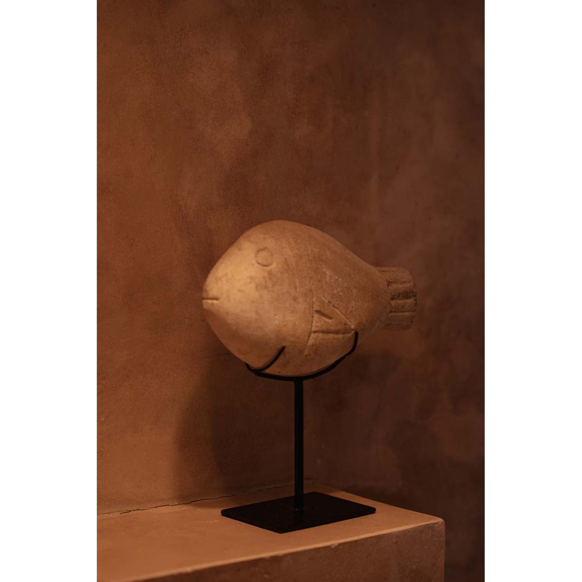 Sculpture poisson en grès vue de trois quarts sur une console enduite dans une lumière chaude
