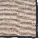 Gros plan sur le tissage rayé en lin de la serviette Code et sa bordure noire cousue