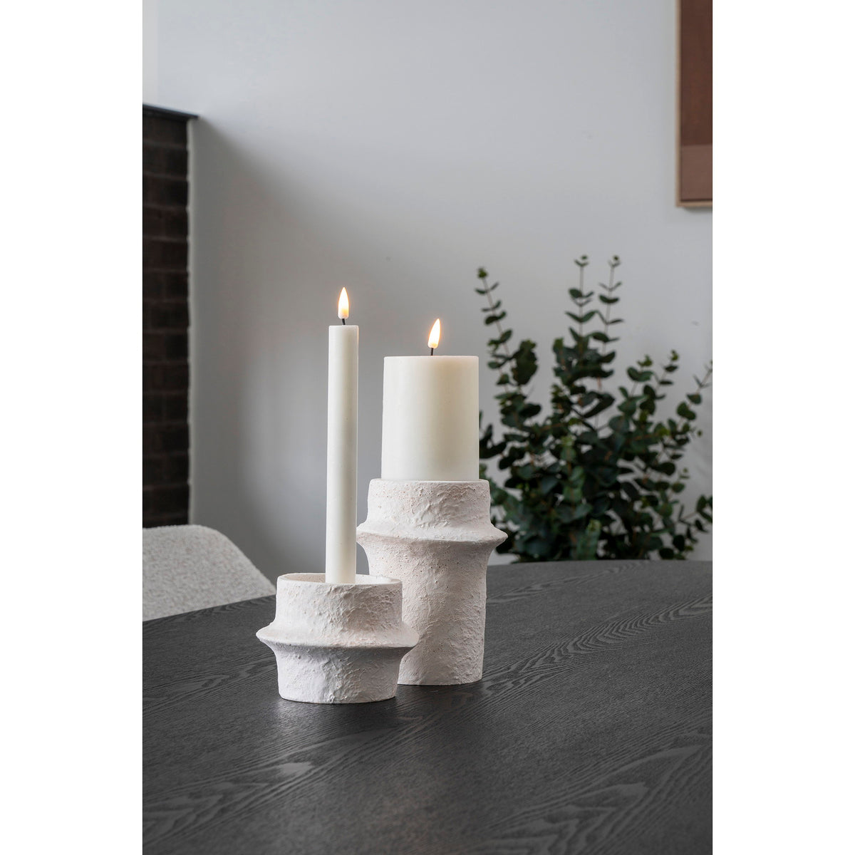 Les deux bougeoirs en ciment blanc sur une table noire avec une bougie chandelle et une bougie pilier allumées